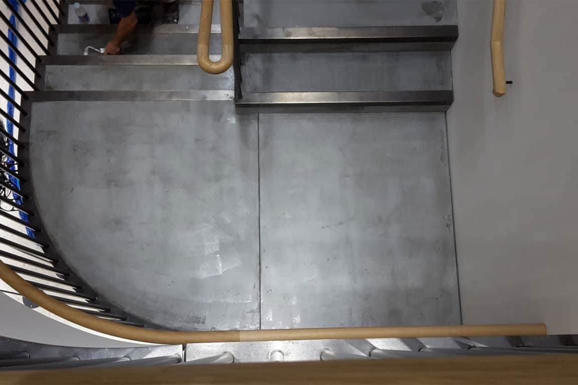 A metal-railed staircase in a building with concrete steps and landing.